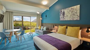 Een hotelkamer met een groot bed, een bank, een eettafel met stoelen en uitzicht op bergen door grote ramen.
