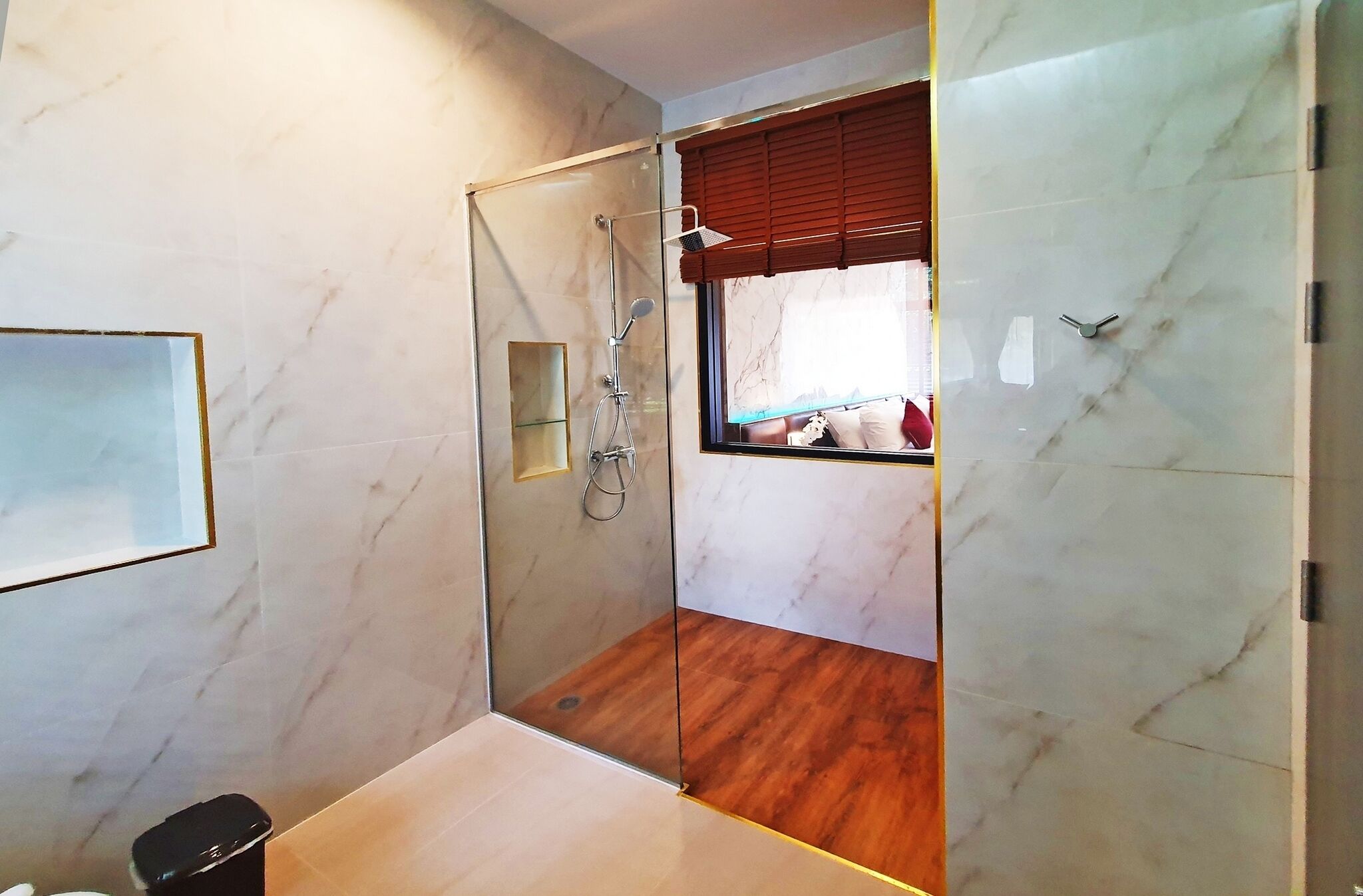 A modern bathroom with a glass shower enclosure, marble walls, and a wooden floor.