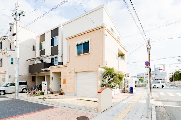 A modern two-story residential building with a garage, a balcony, and a small garden area.