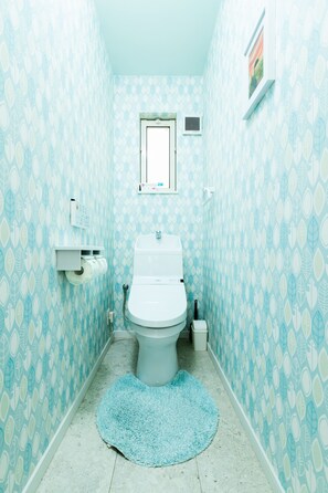 A bathroom with a toilet, a small window, a calendar, and a patterned wall.