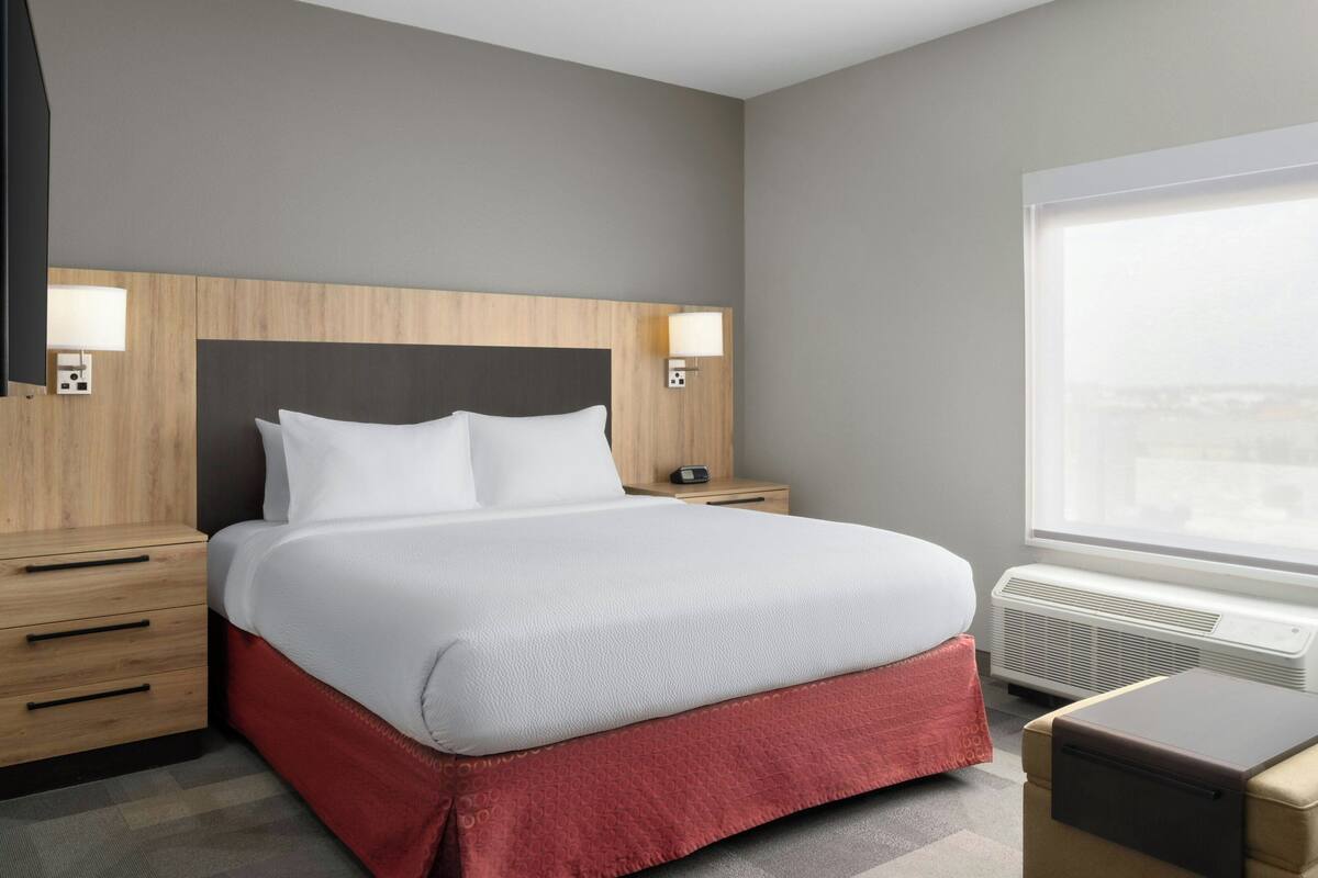 Een hotelkamer met een groot bed, nachtkastjes, een verwarming en een raam met uitzicht.