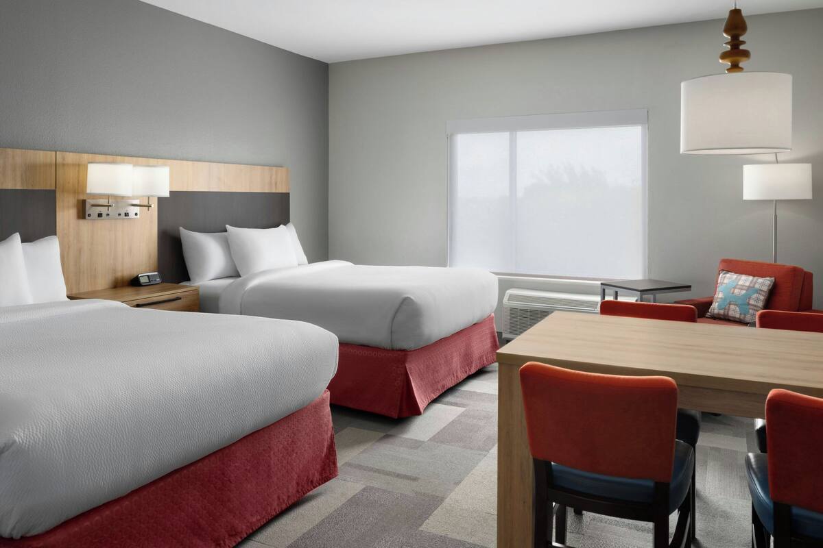 Een hotelkamer met twee bedden, een eettafel en stoelen. Er is een raam met uitzicht op het exterieur.