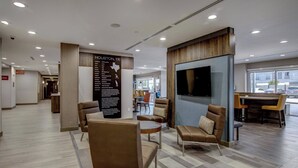A modern hotel lobby with seating areas, a reception desk, and a large wall-mounted TV. - Towneplace Suites Houston Hobby Airport (Houston)