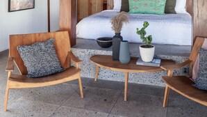 A bedroom with a wooden ceiling, a bed with green and white pillows, a small table with a potted plant, and two wooden chairs. - Mandala The Bay (Lembongan Island)