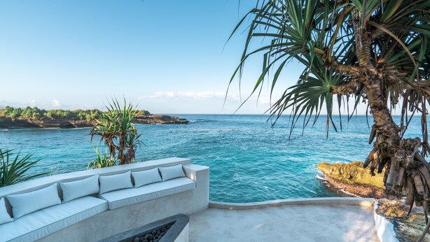 A coastal terrace with a seating area overlooking the sea, a palm tree, and rocky terrain. - Mandala The Bay (Lembongan Island)