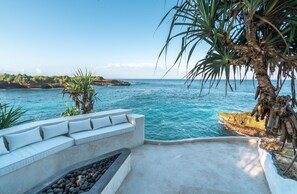 A coastal terrace with a seating area overlooking the sea, a palm tree, and rocky terrain. - Mandala The Bay (Lembongan Island)
