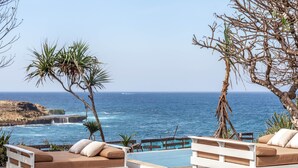 A poolside area with two white sofas and a wooden deck overlooking the ocean. - Mandala The Bay (Lembongan Island)