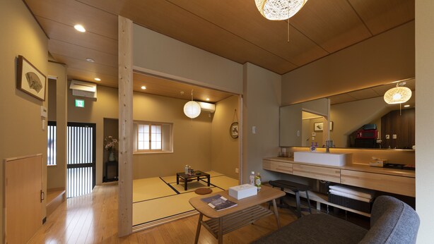 Une pièce de style japonais traditionnel, avec un sol recouvert de tatamis, une petite table basse avec un coussin, un canapé et un grand miroir.