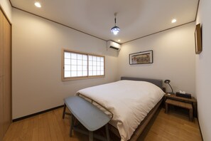 A bedroom with a bed, a bench, a bedside table, a wall-mounted air conditioner, a window, and a framed picture. - Shirakabanoyado-Siokusa (Osaka)