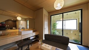 Une cuisine moderne avec un plan de travail en bois, un coin repas avec un banc et une grande fenêtre donnant sur une clôture en bambou.