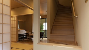 Un escalier en bois muni d’une rampe, menant à une pièce dont le sol est recouvert de tatamis et qui est dotée d’une porte coulissante traditionnelle.