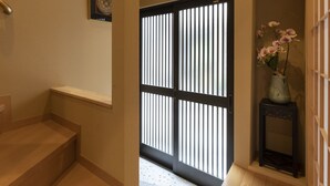 Un couloir avec des marches en bois, une porte coulissante noire et une petite table sur laquelle est posé un vase de fleurs.