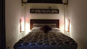 Un lit avec une couvre-lit à motifs, une tête de lit en bois et des appliques murales de chaque côté.