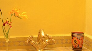 Un lavabo de salle de bain avec un seul robinet, un vase en verre avec des fleurs et une tasse décorative.