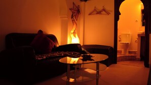 Un salon faiblement éclairé, avec un canapé, une table basse en verre et une cheminée.