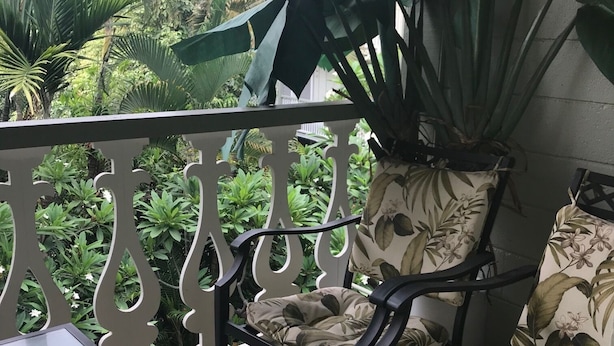 Ein Balkon mit Tisch, zwei Stühlen mit floralem Bezug und großen Kübelpflanzen.