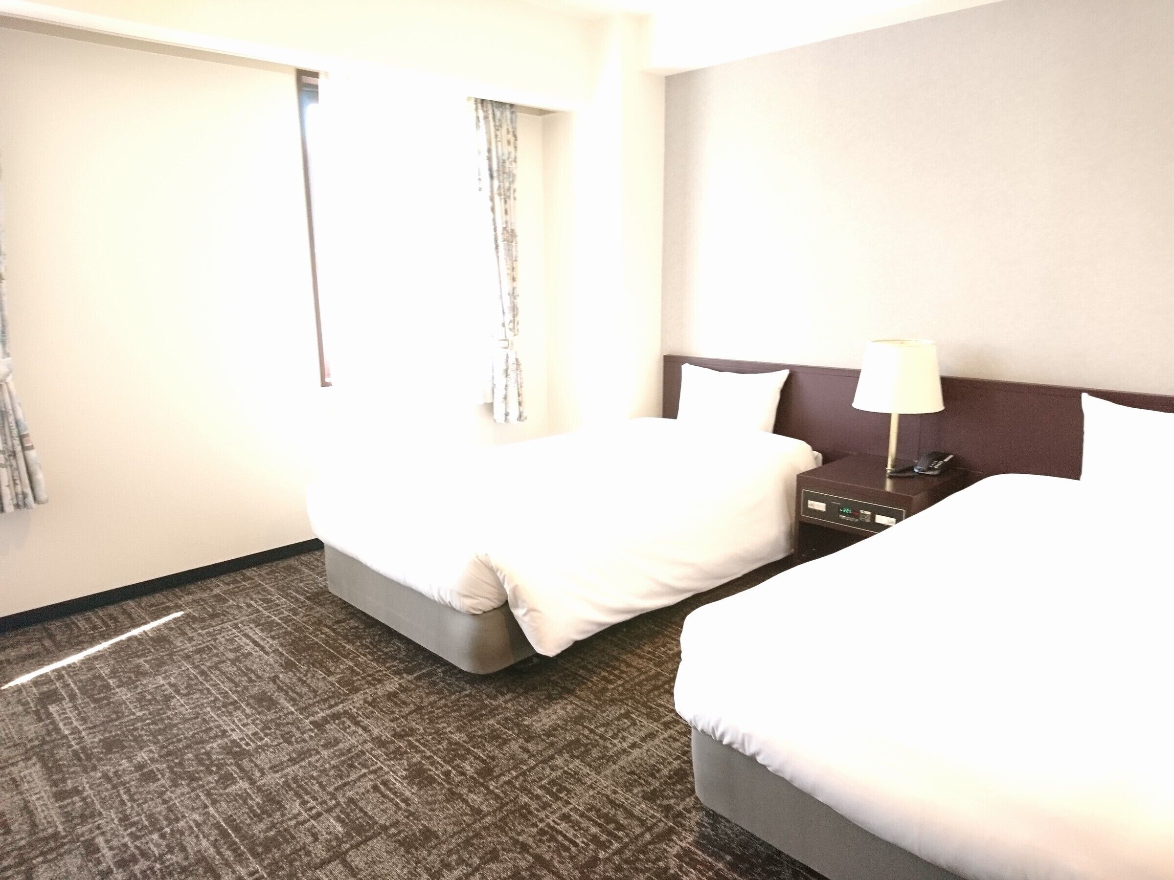 Ein Hotelzimmer mit zwei Betten, einem Nachttisch, einer Lampe und einer Wanduhr.