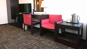 Ein Hotelzimmer mit Schreibtisch, zwei Stühlen, Fernseher, Spiegel, Lampe und einer Kaffeemaschine.