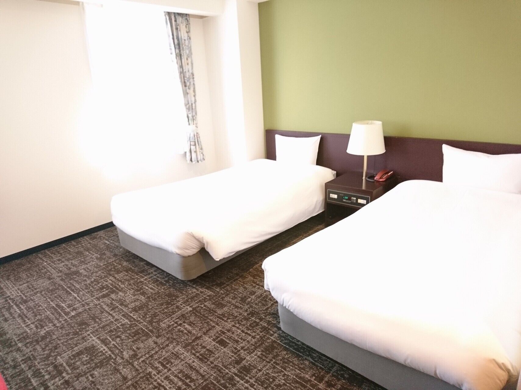 Ein Hotelzimmer mit zwei Betten, einem Nachttisch mit Lampe und einem Fenster mit Vorhängen.