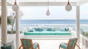 Eine Strandlounge mit Blick auf das Meer, einer weißen Decke und zwei Korbstühlen mit Kissen.