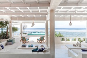 A spacious outdoor lounge area with a view of the ocean, featuring a white ceiling, hanging light fixtures, and comfortable seating. - Mandala The Rocks (Pecatu)
