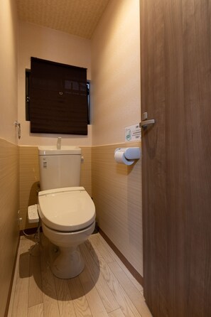 A small, compact bathroom with a toilet, a wall-mounted sink, and a wooden door. - Shirakabanoyado-Tennoji (Osaka)