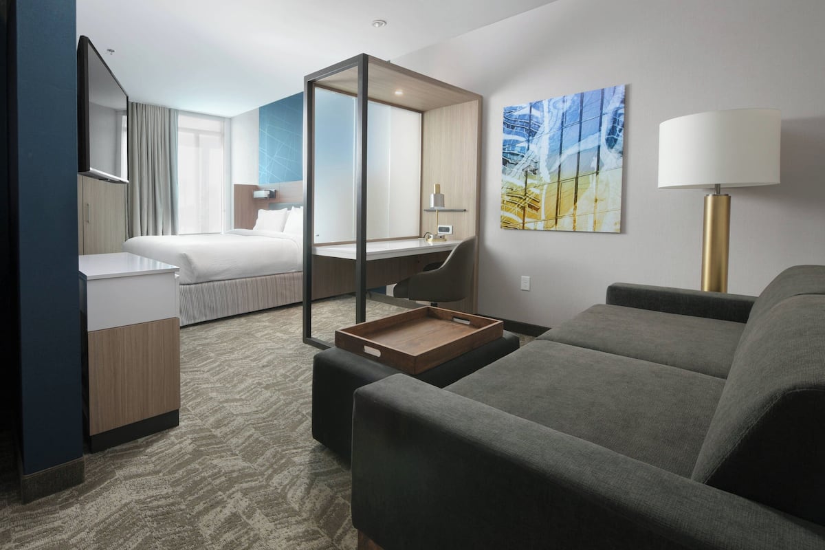 Una habitación de hotel con cama, escritorio, sofá y un espejo grande.