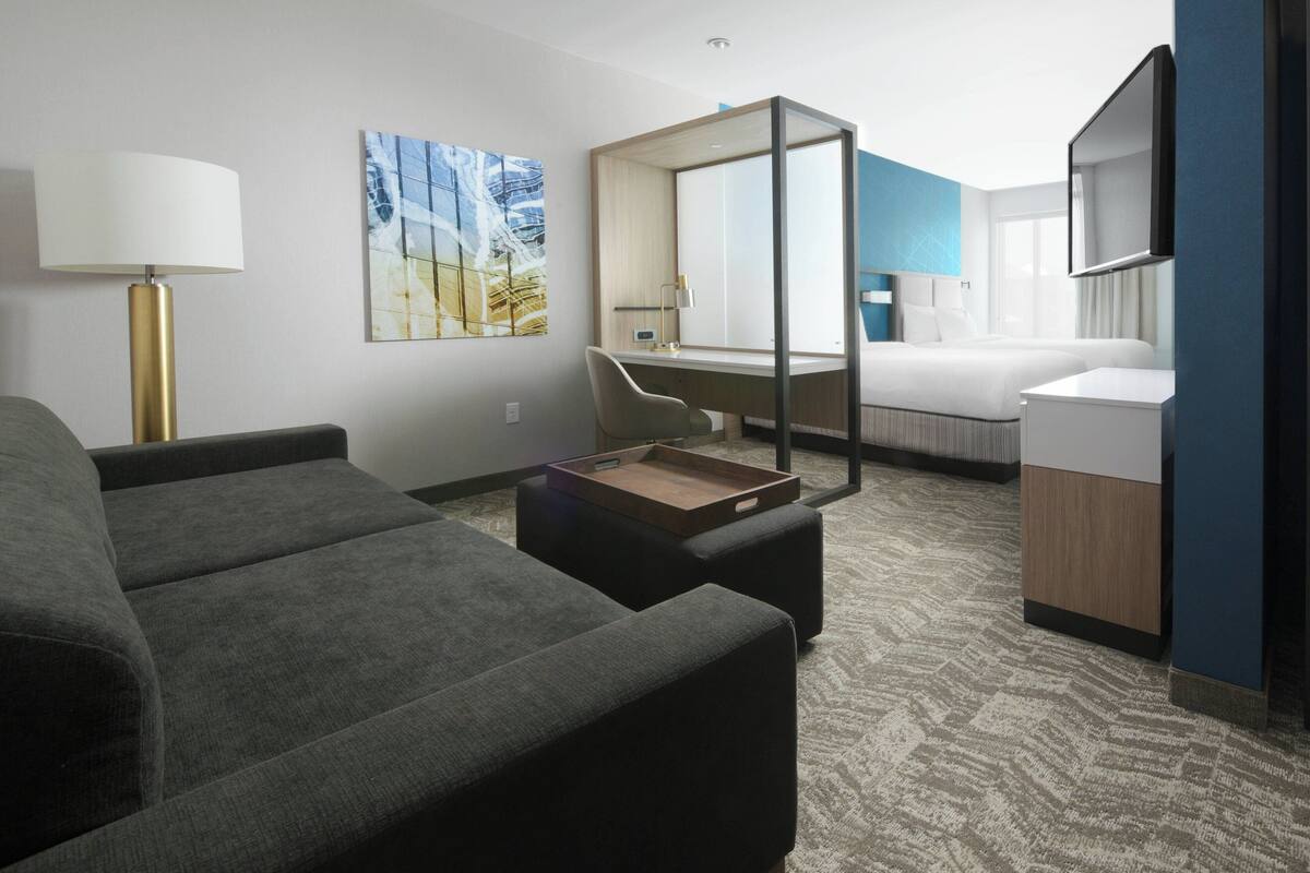 Una habitación de hotel moderna con sofá, escritorio, cama y un espejo grande.