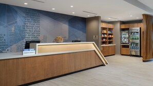 A hotel reception area with a wooden reception desk, a wall with text, and a refrigerator with beverages. - SpringHill Suites by Marriott Texas City (Texas City)