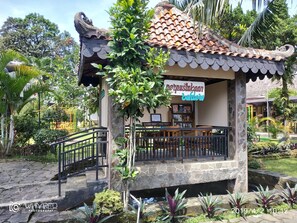 A traditional-style building with a tiled roof and a signboard, surrounded by lush greenery and a stone pathway. - Hotel Bahtera PT.Pelni (Megamendung)