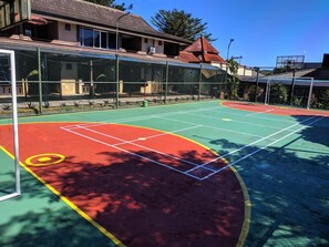 An outdoor tennis court with a green and red surface, surrounded by a chain-link fence, and adjacent to a building with a tiled roof. - Hotel Bahtera PT.Pelni (Megamendung)