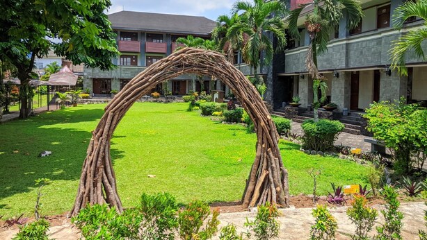 A courtyard with a natural archway, lush greenery, and a building with a stone facade and multiple windows. - Hotel Bahtera PT.Pelni (Megamendung)