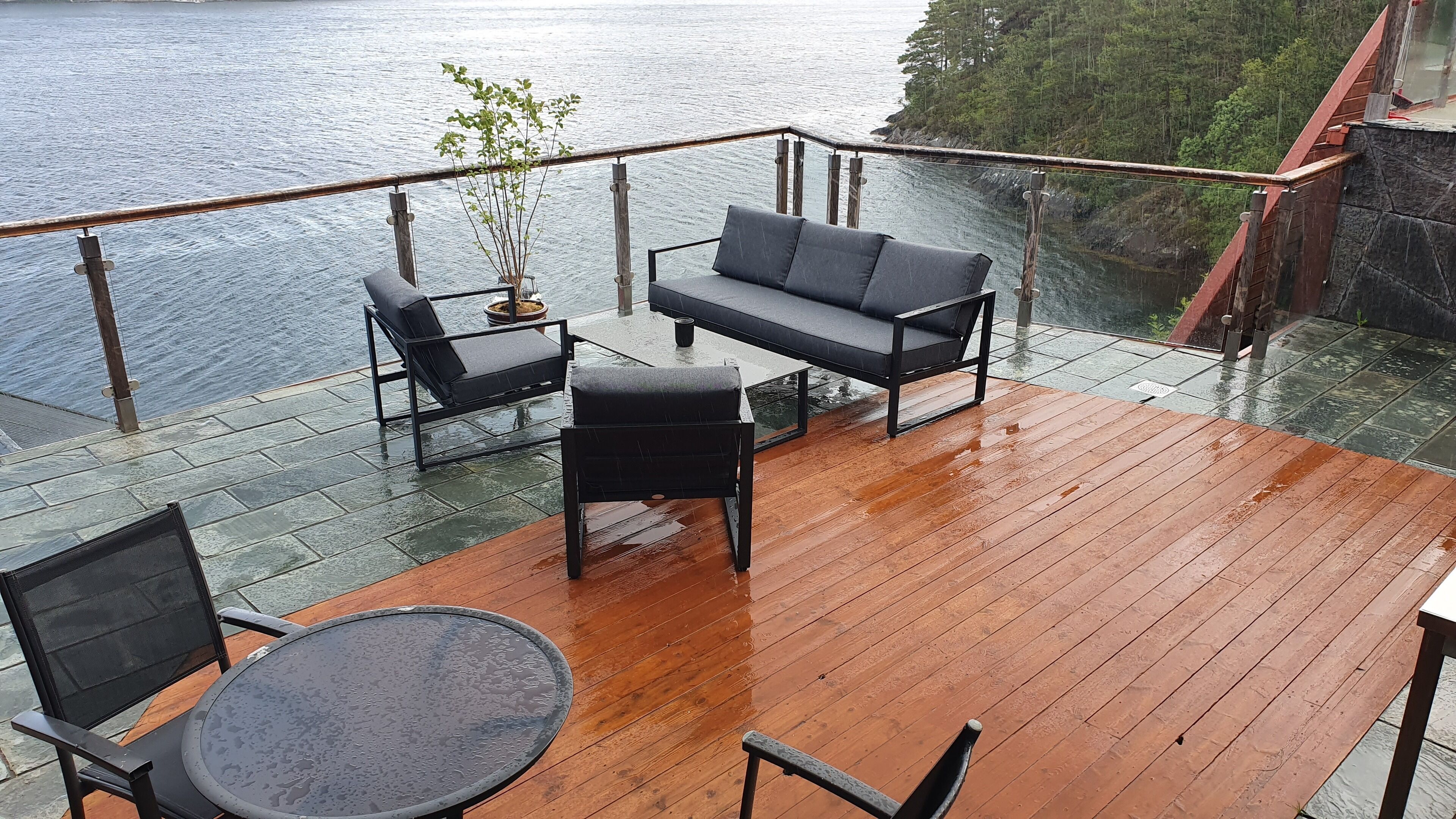 Une terrasse en bois, aménagée avec du mobilier d’extérieur, notamment un canapé et des fauteuils, donnant sur une étendue d’eau.