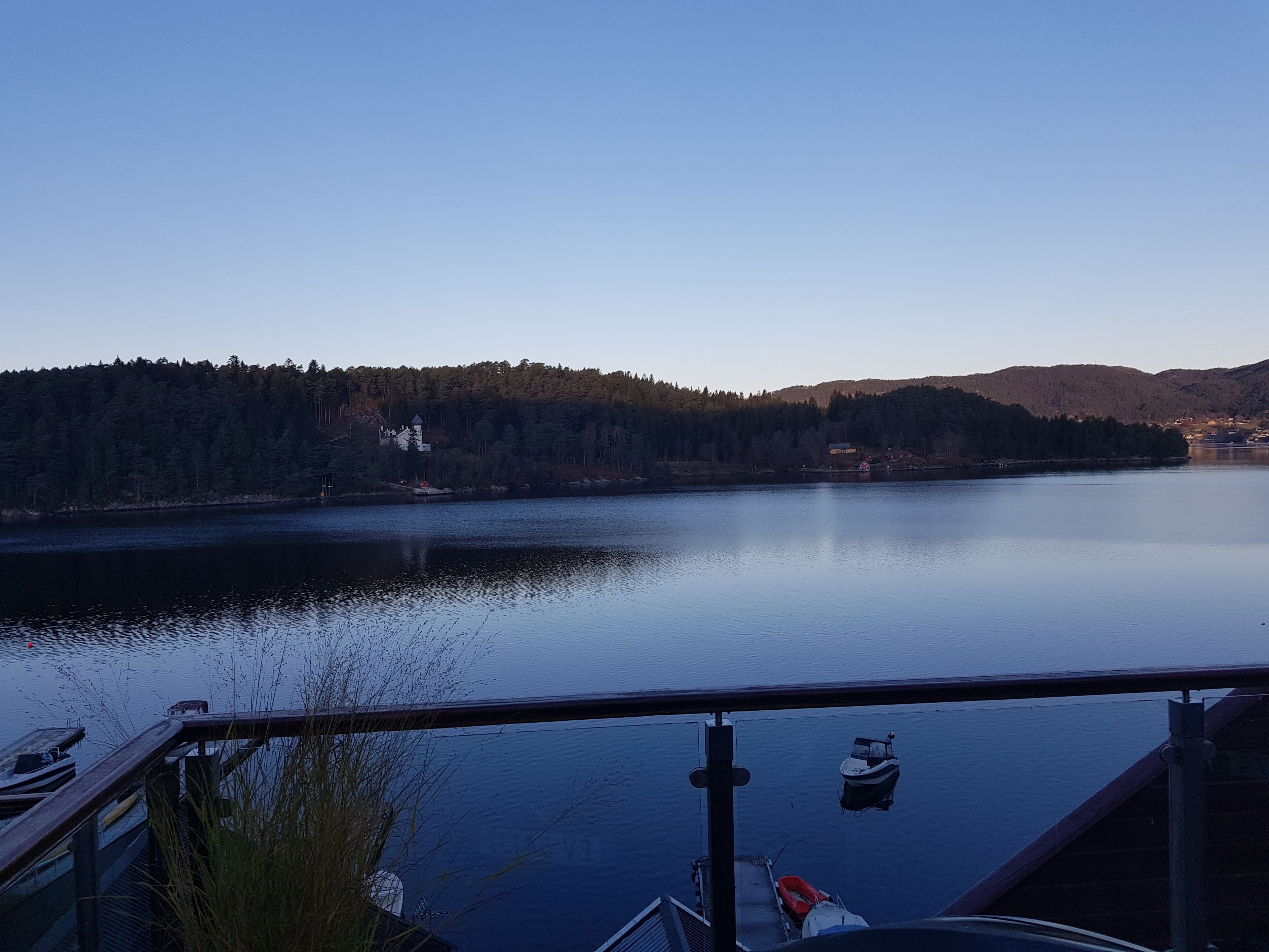 A lake with a dock and boats, surrounded by forested hills and a clear sky.