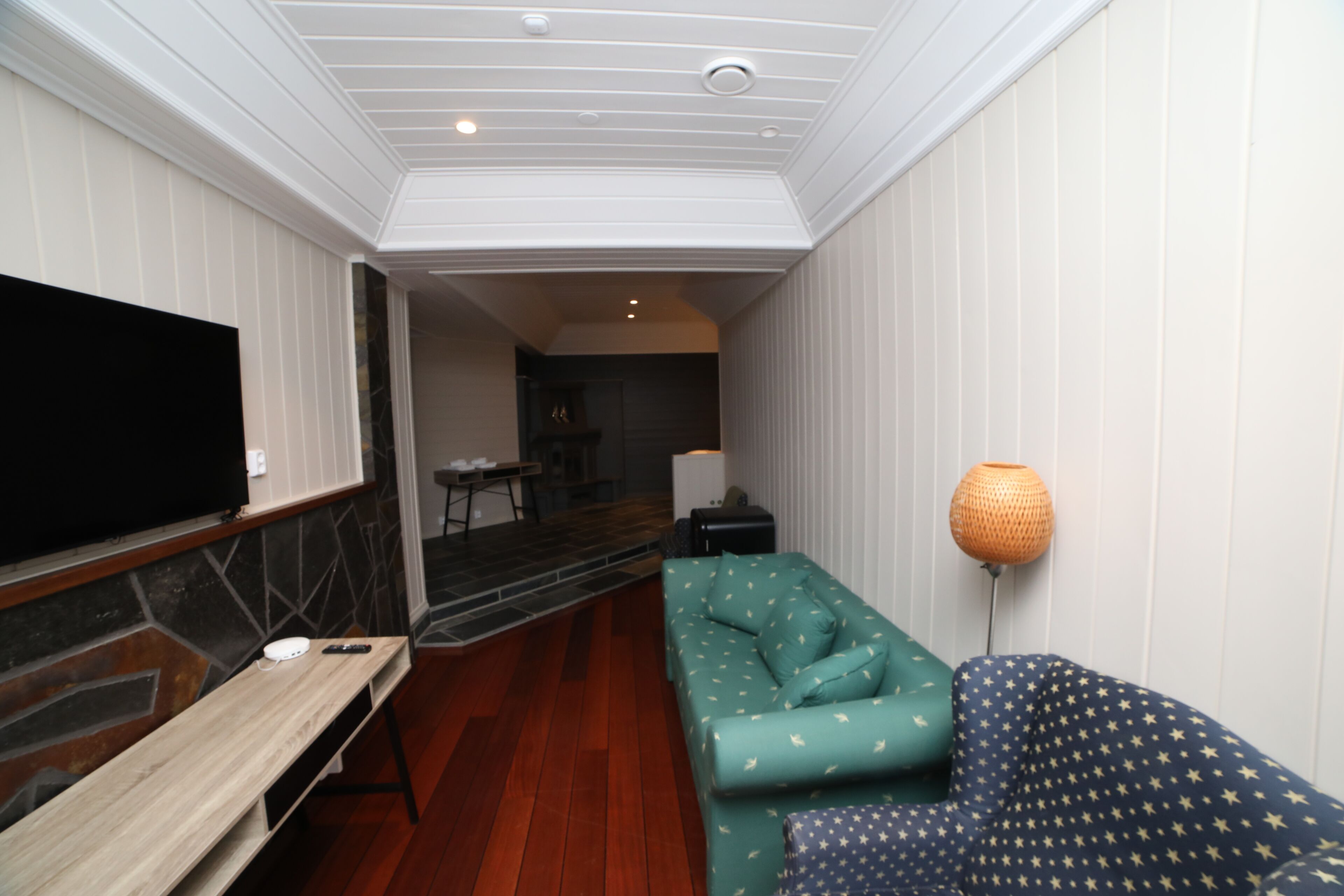 A modern living room with a wooden bench, a teal sofa, and a TV mounted on the wall.
