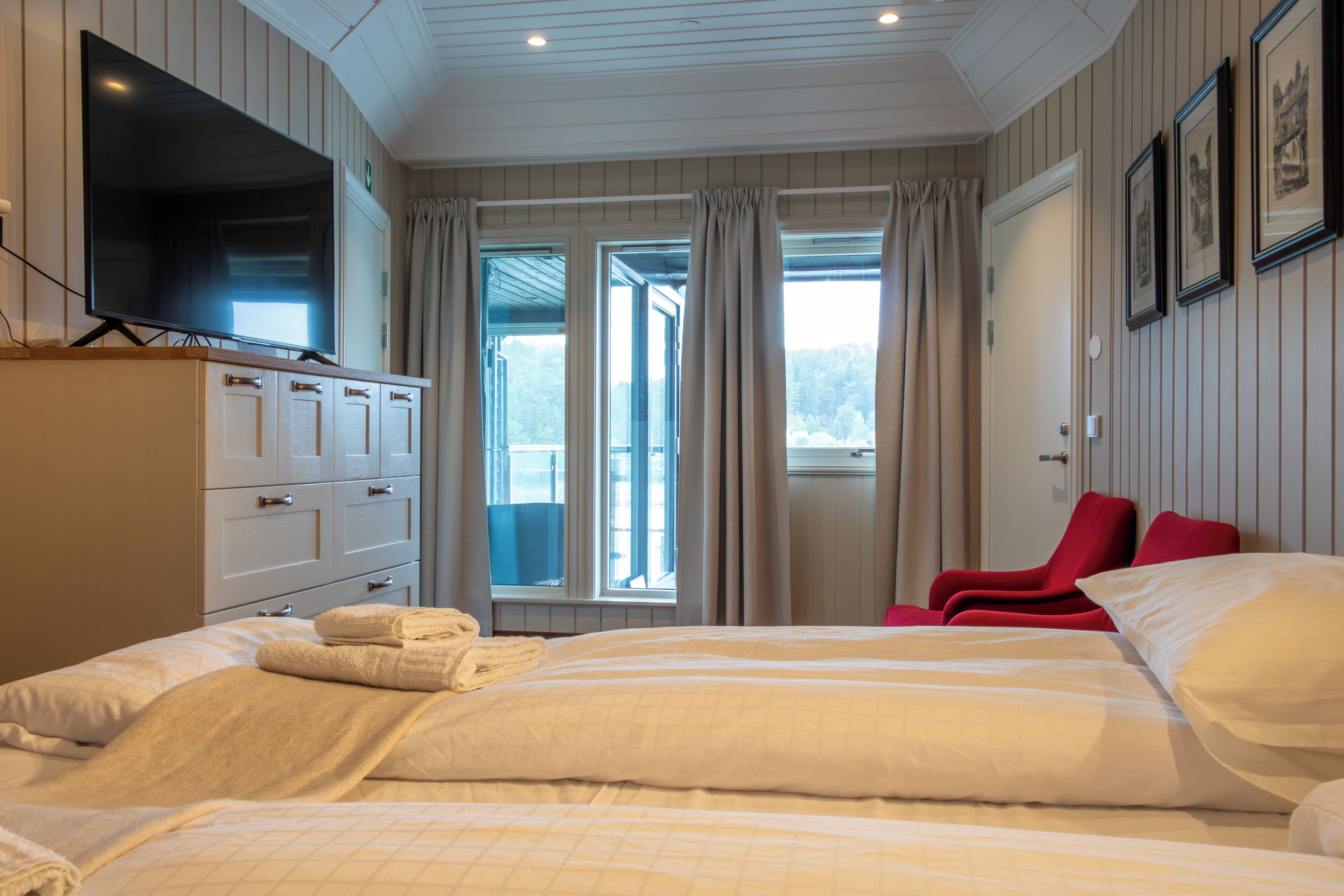 Ein Hotelzimmer mit Bett, Fernseher, Schreibtisch mit Schubladen, Stuhl und einem Fenster mit Vorhängen.