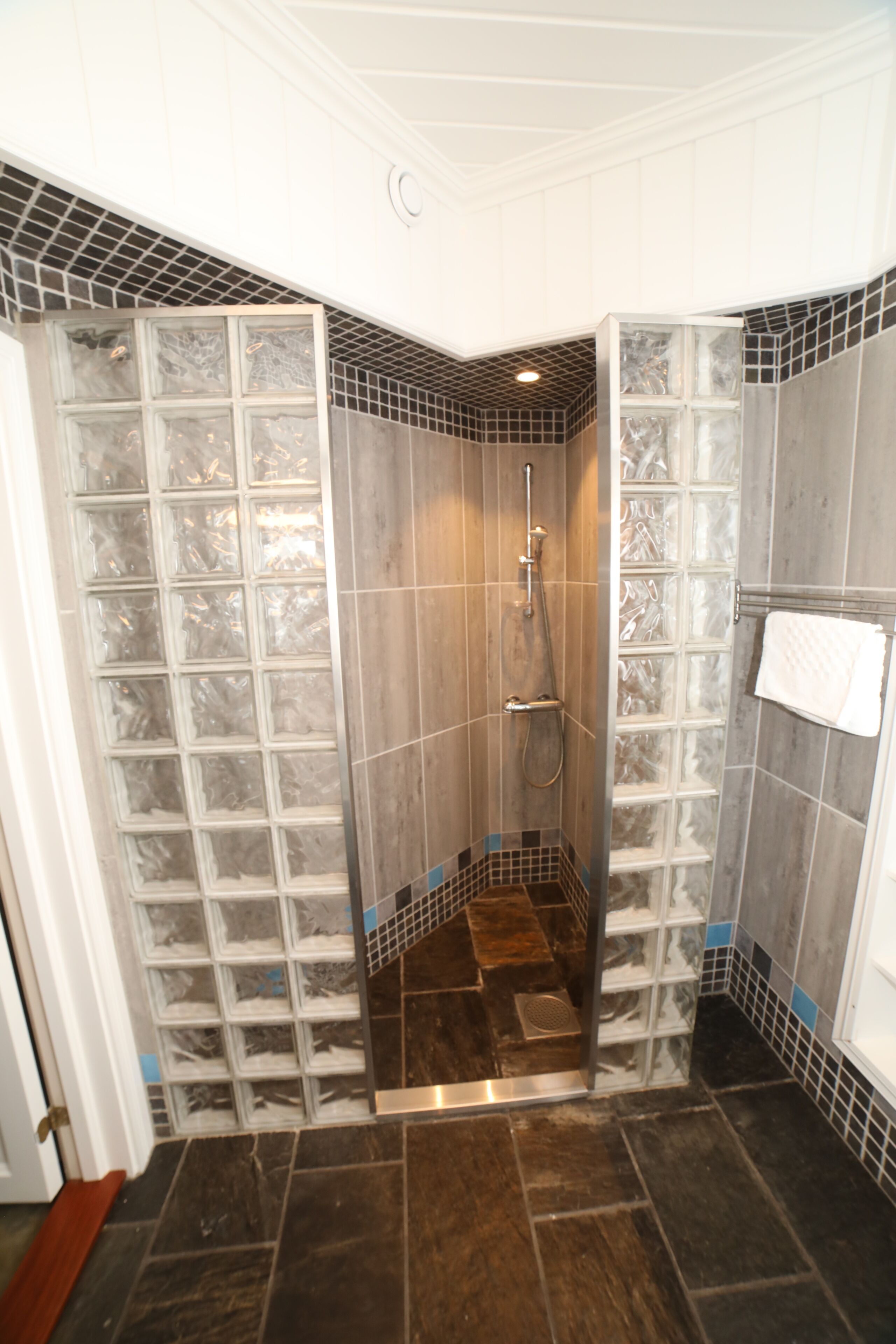 Een douche met een glazen deur, betegelde wanden en een donkere vloer.
