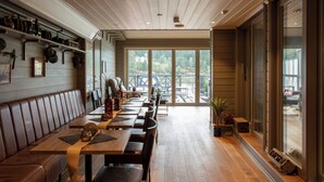 Um restaurante com mesas e bancos de madeira, janelas amplas e vista para o exterior.