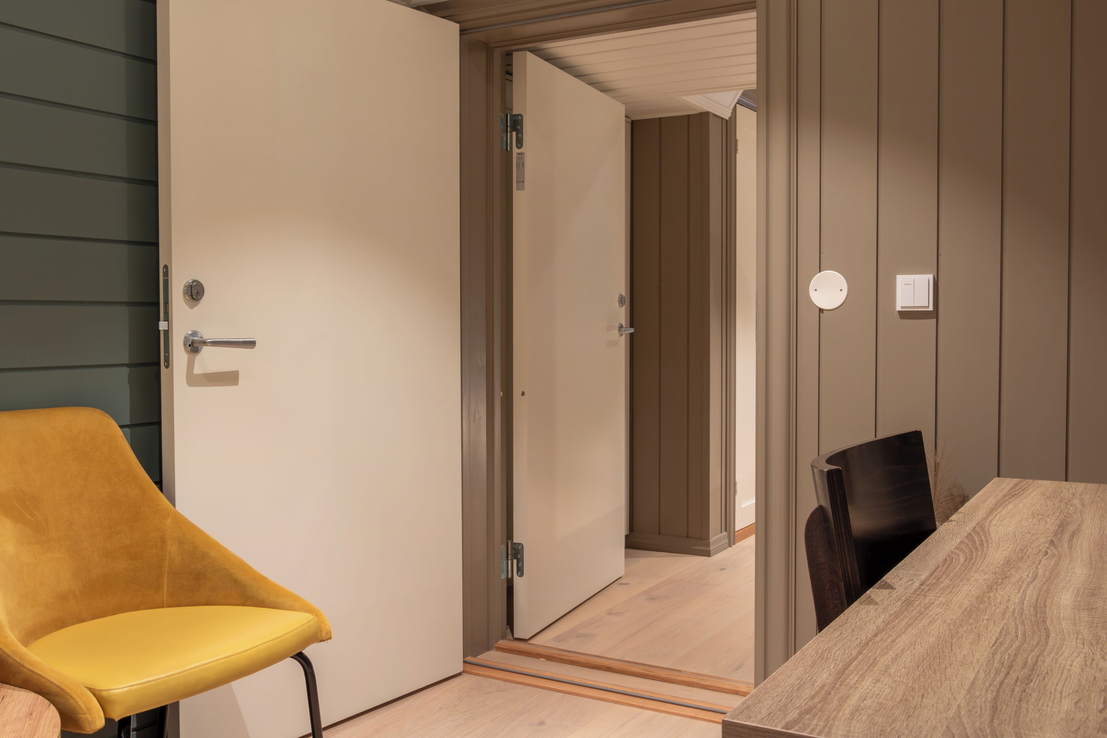 A room with a wooden table, a yellow chair, and a door leading to another room.