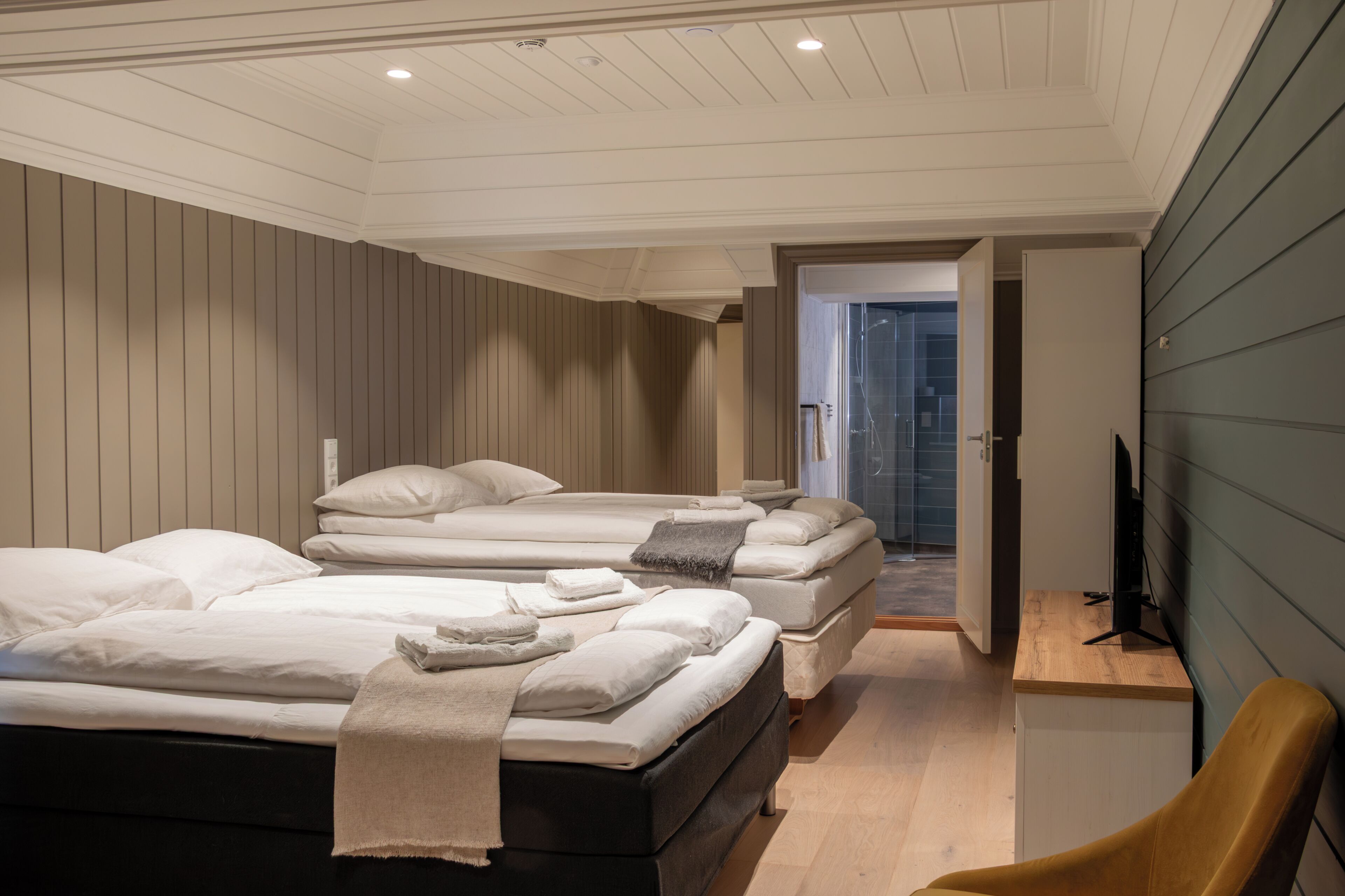 Habitación de hotel con tres camas, suelo de madera, televisor y escritorio.