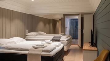 Habitación de hotel con tres camas, suelo de madera, televisor y escritorio.