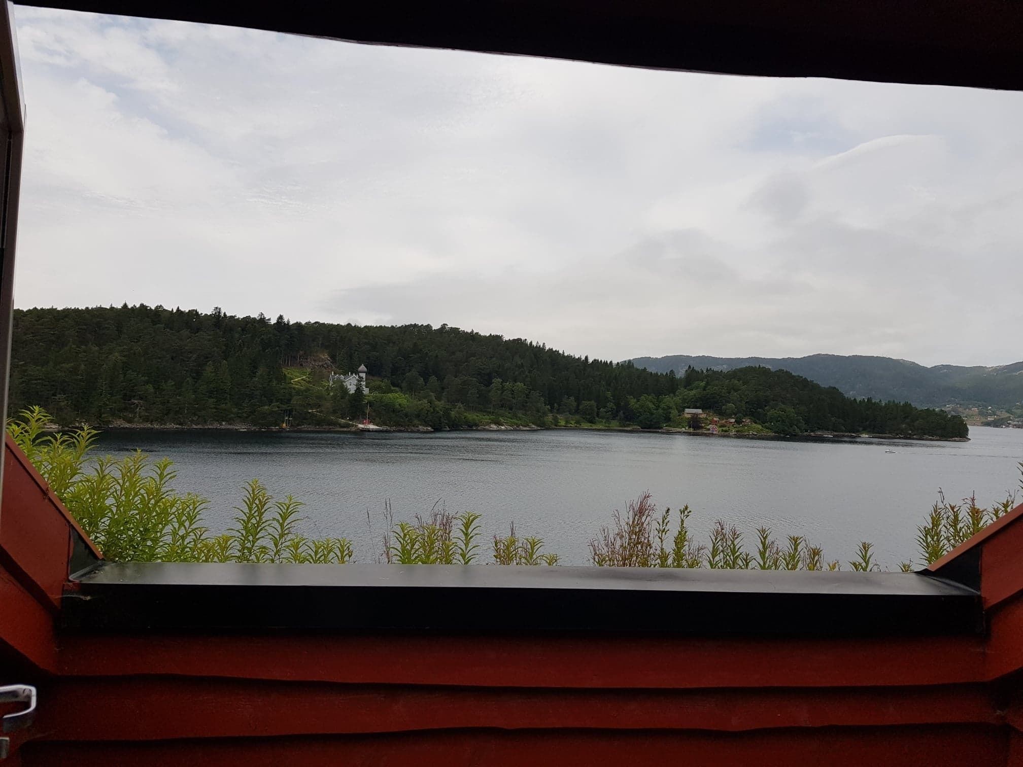 A view from a window overlooking a lake with a forested island and distant hills.