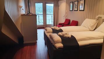 A hotel room with two beds, a desk, a red chair, and a view of a forest through the window.