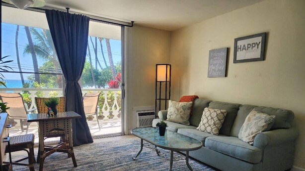 A living room with a sofa, a coffee table, and a chair. There is a view of the outdoors through a sliding door.