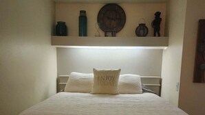 A neatly made bed with a white bedspread and a pillow with the text "ENJOY TODAY".