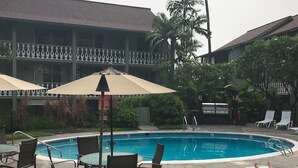 A swimming pool area with lounge chairs and umbrellas, surrounded by a fence and greenery.