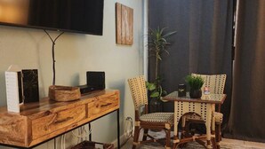 A cozy living room with a flat-screen TV mounted on the wall, a wooden coffee table, wicker chairs, and a small potted plant.