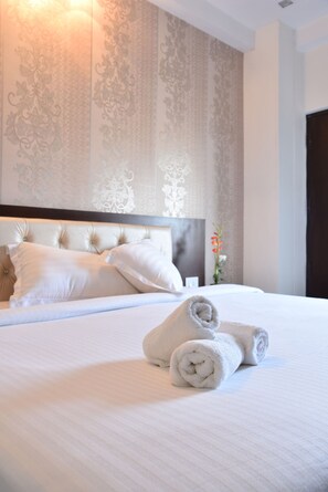 A neatly made bed with rolled towels, a headboard, and a wall with a floral pattern. - Hotel FloraInn (Gurugram)