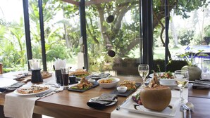 A dining table set with various dishes, glasses, and cutlery, overlooking a lush garden. - Beachfront villa with pool and full staff (Maggona)