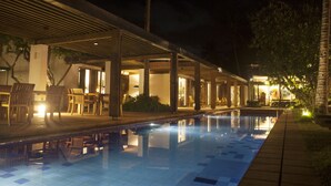 A nighttime swimming pool area with a covered seating area and a well-lit patio. - Beachfront villa with pool and full staff (Maggona)